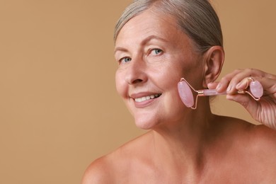 Beautiful woman doing facial massage with roller on beige background