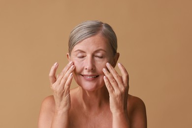 Beautiful woman doing facial massage on beige background