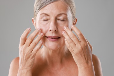 Photo of Beautiful woman doing facial massage on grey background