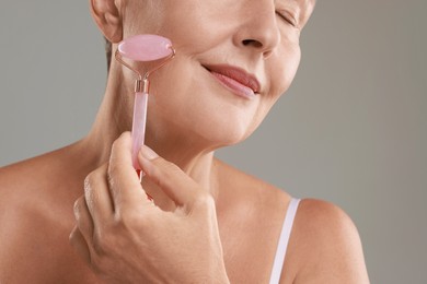 Photo of Woman doing facial massage with roller on grey background, closeup