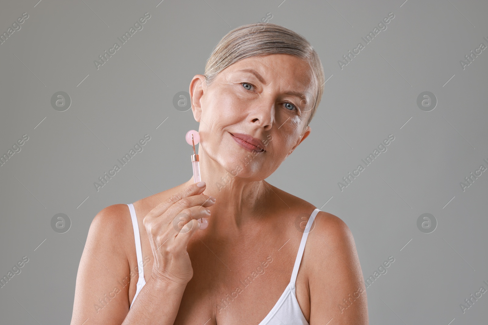 Photo of Beautiful woman doing facial massage with roller on grey background