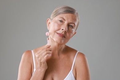 Beautiful woman doing facial massage with roller on grey background