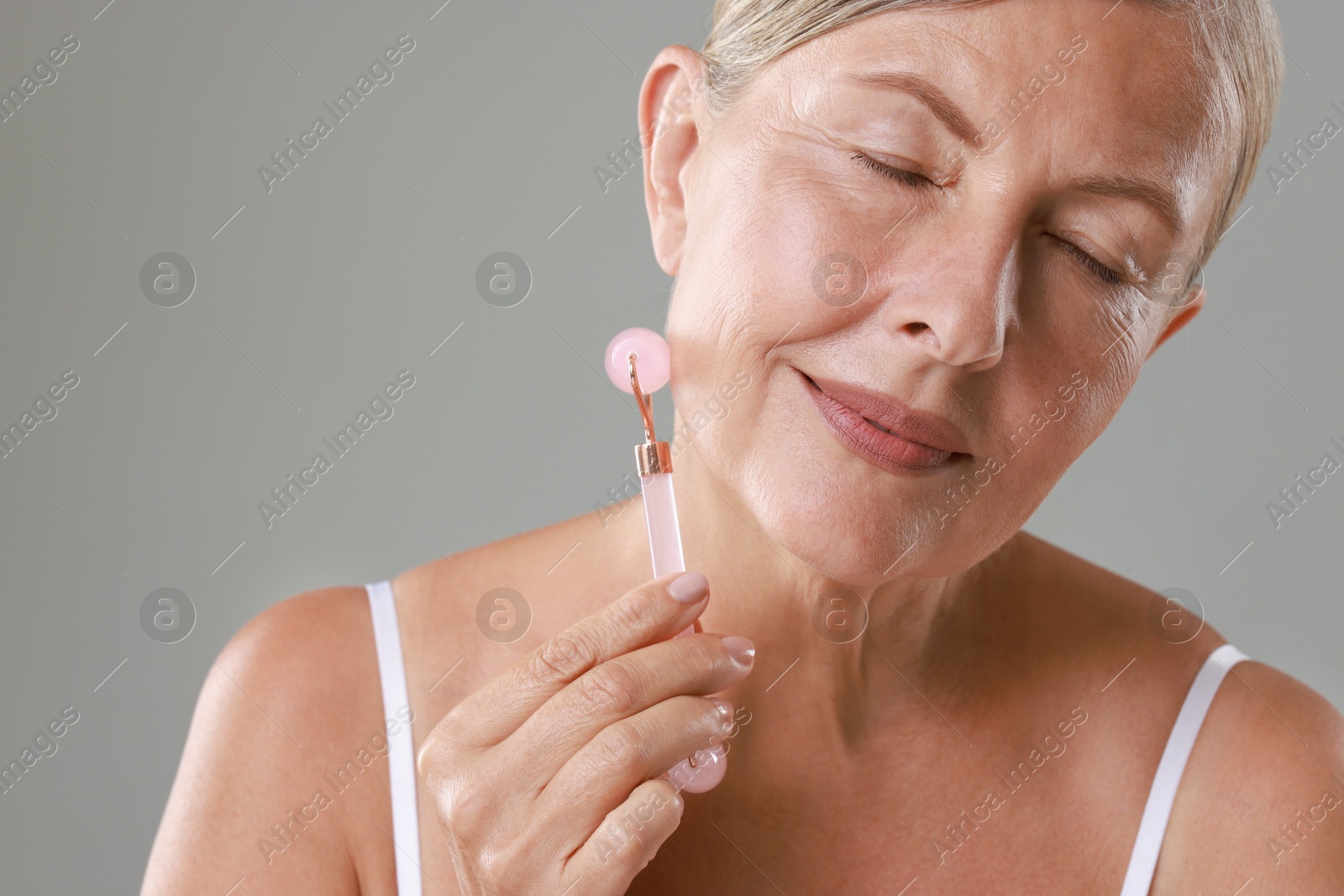 Photo of Beautiful woman doing facial massage with roller on grey background