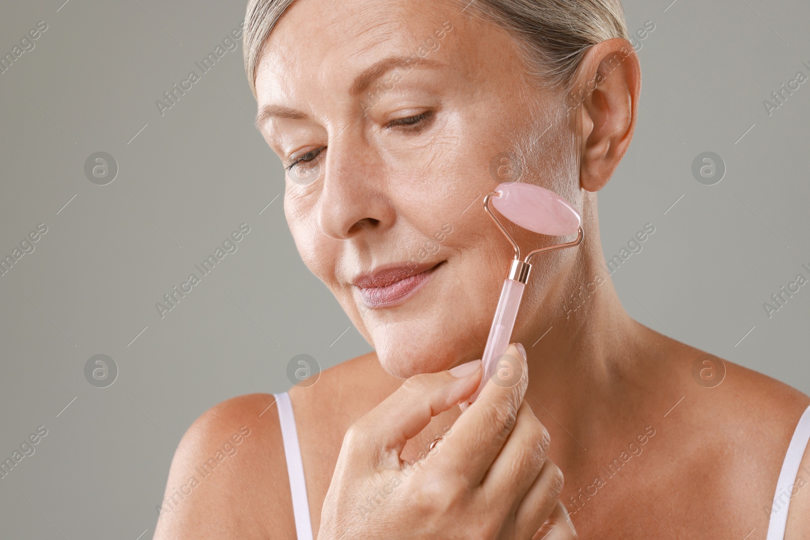 Photo of Beautiful woman doing facial massage with roller on grey background