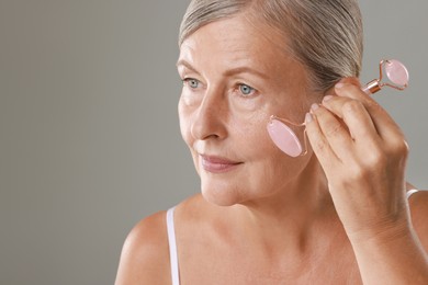 Photo of Beautiful woman doing facial massage with roller on grey background