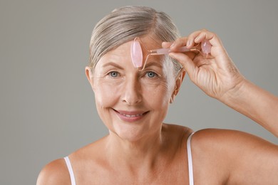 Photo of Beautiful woman doing facial massage with roller on grey background