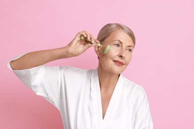 Photo of Beautiful woman doing facial massage with roller on pink background