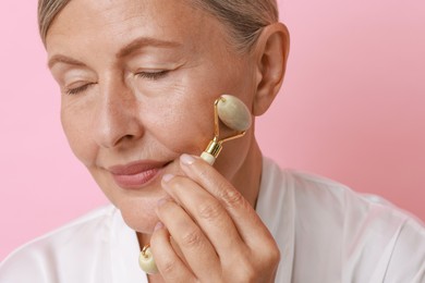 Photo of Beautiful woman doing facial massage with roller on pink background, closeup