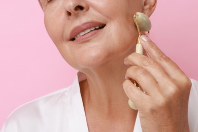 Woman doing facial massage with roller on pink background, closeup