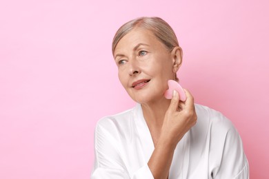 Photo of Beautiful young woman doing facial massage with gua sha tool on pink background