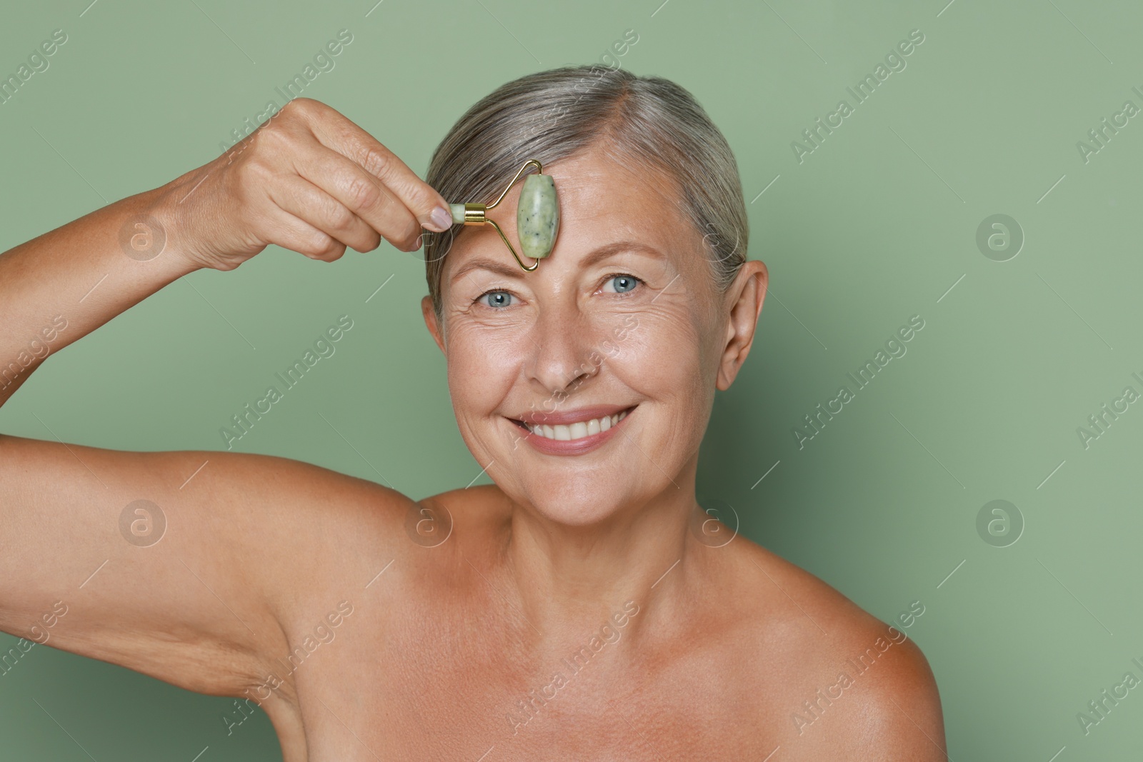 Photo of Beautiful woman doing facial massage with roller on light green background