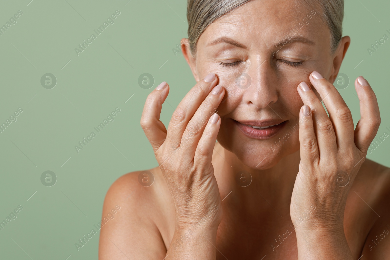 Photo of Beautiful woman doing facial massage on light green background