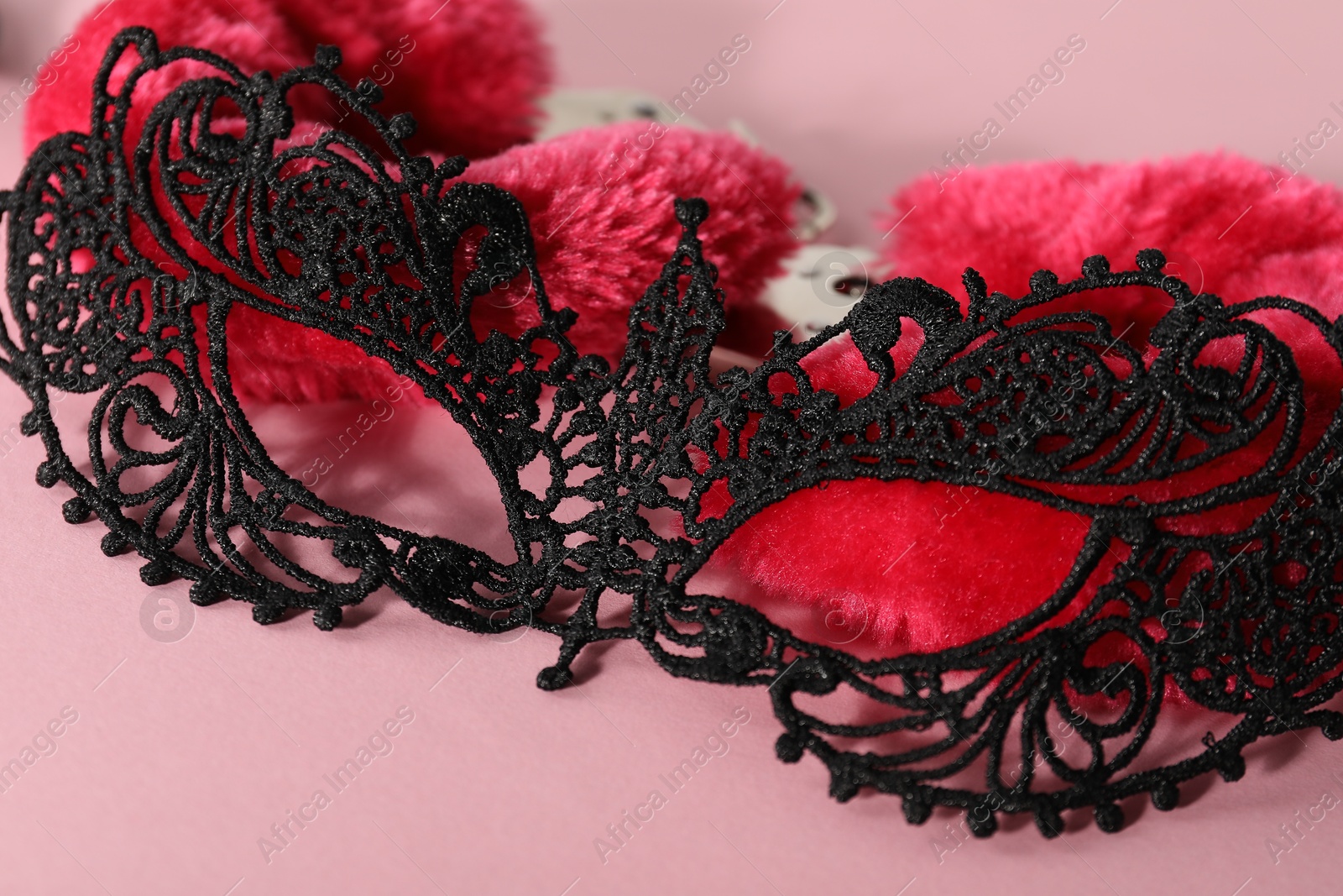 Photo of Lace mask and fluffy handcuffs on pink background, closeup