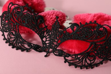 Lace mask and fluffy handcuffs on pink background, closeup