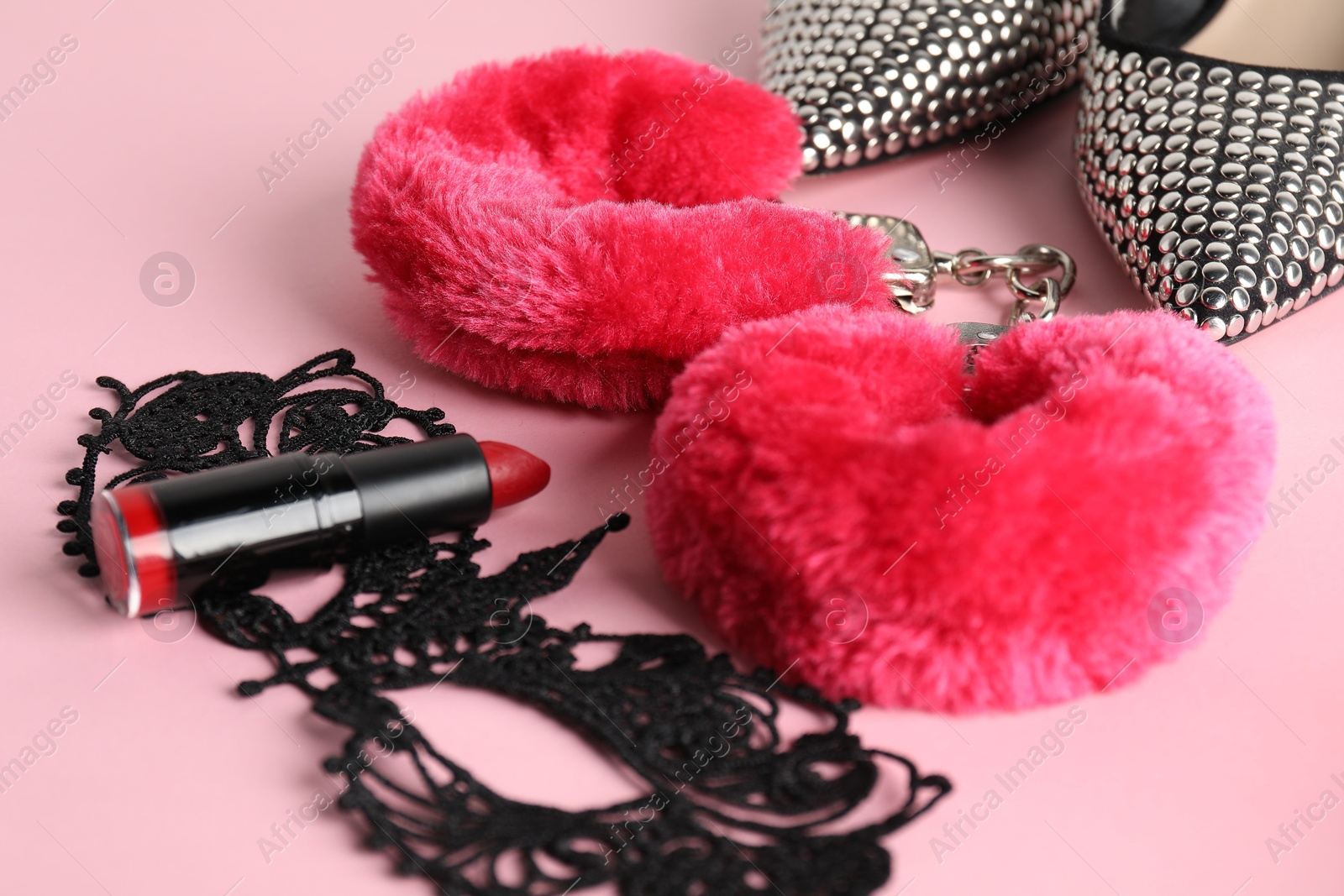 Photo of Fluffy handcuffs, lace mask, high-heeled shoes and lipstick on pink background, closeup