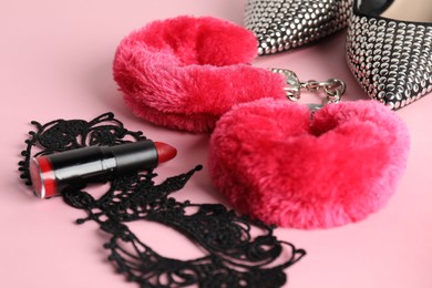 Photo of Fluffy handcuffs, lace mask, high-heeled shoes and lipstick on pink background, closeup