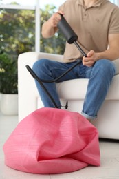 Photo of Man inflating fitness ball with manual pump indoors, closeup