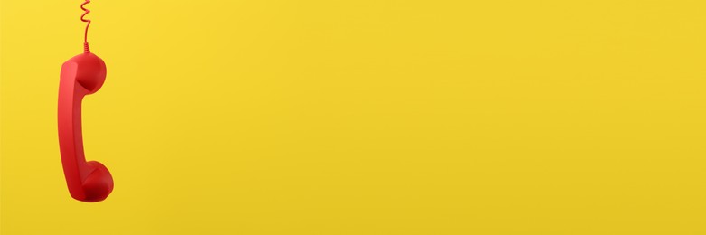 Image of Red corded telephone handset on yellow background. Banner design with space for text