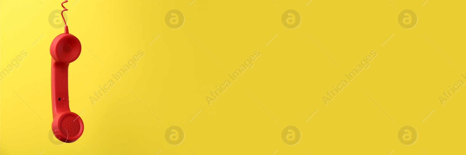 Image of Red corded telephone handset on yellow background. Banner design with space for text