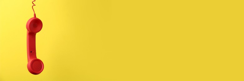 Image of Red corded telephone handset on yellow background. Banner design with space for text