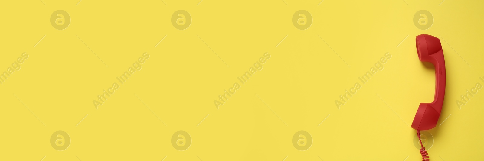 Image of Red corded telephone handset on yellow background, top view. Banner design with space for text