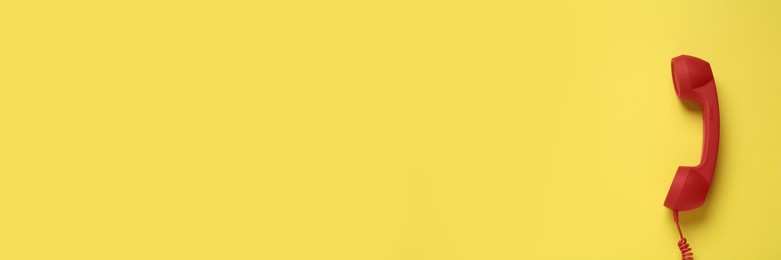 Image of Red corded telephone handset on yellow background, top view. Banner design with space for text