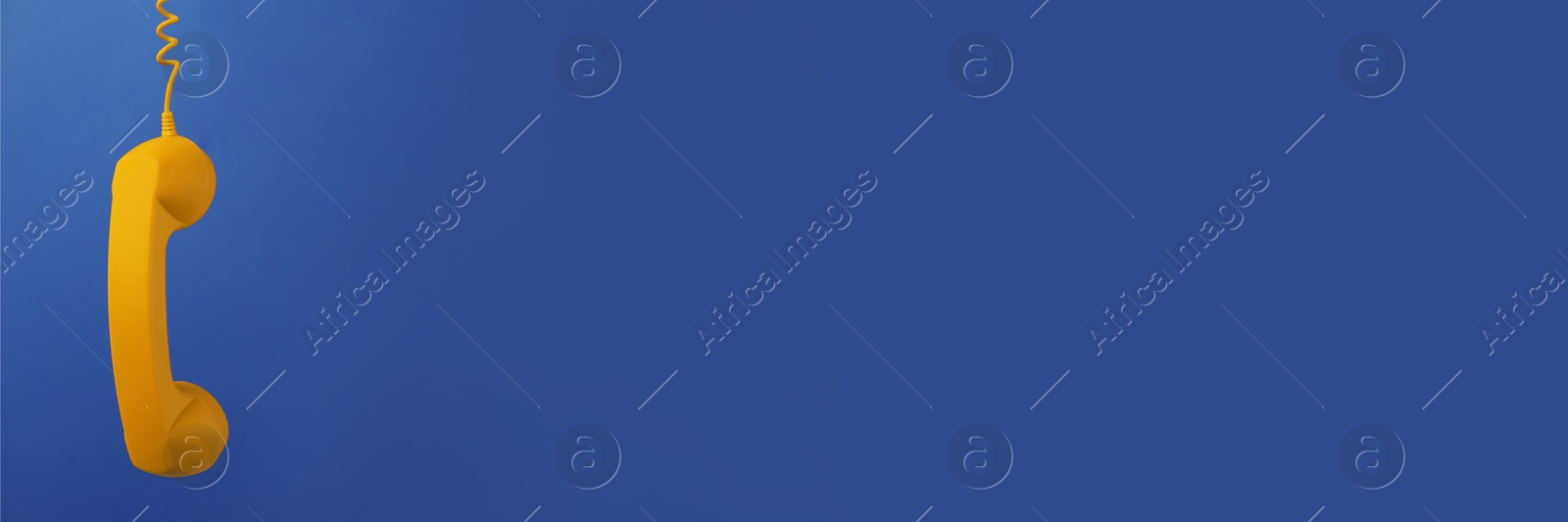 Image of Yellow corded telephone handset on blue background. Banner design with space for text