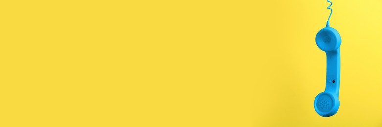 Image of Light blue corded telephone handset on yellow background. Banner design with space for text