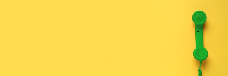 Green corded telephone handset on yellow background, top view. Banner design with space for text