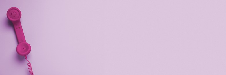 Image of Magenta color telephone handset on violet background, top view. Banner design with space for text