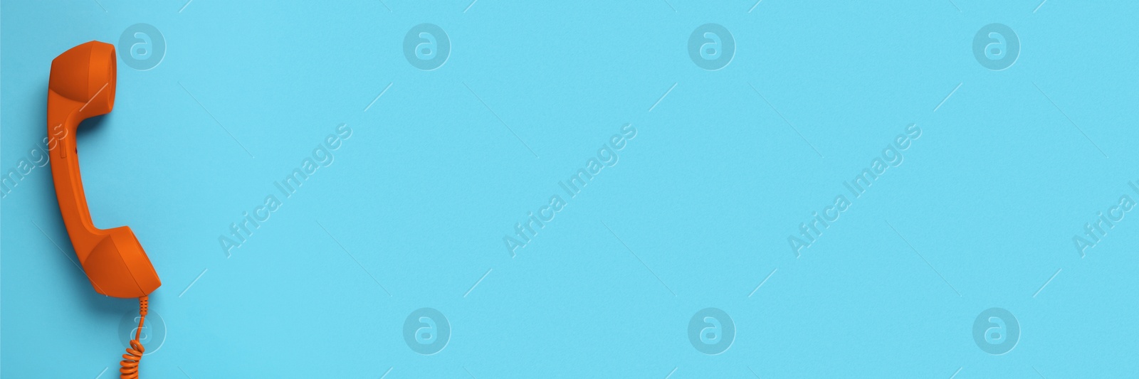 Image of Orange corded telephone handset on light blue background, top view. Banner design with space for text