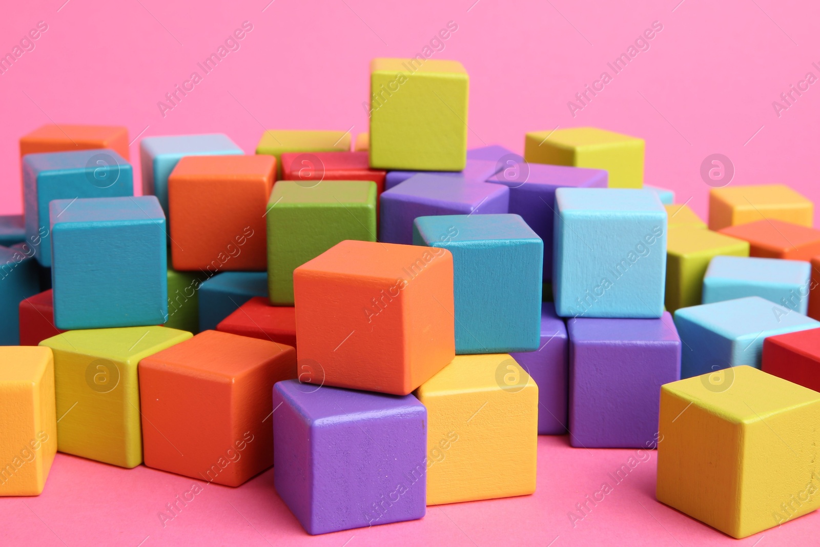 Photo of Many wooden colorful cubes on pink background, closeup