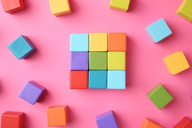 Photo of Many wooden colorful cubes on pink background, top view