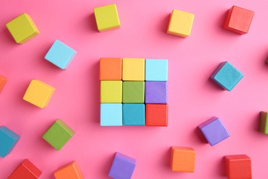 Photo of Many wooden colorful cubes on pink background, top view