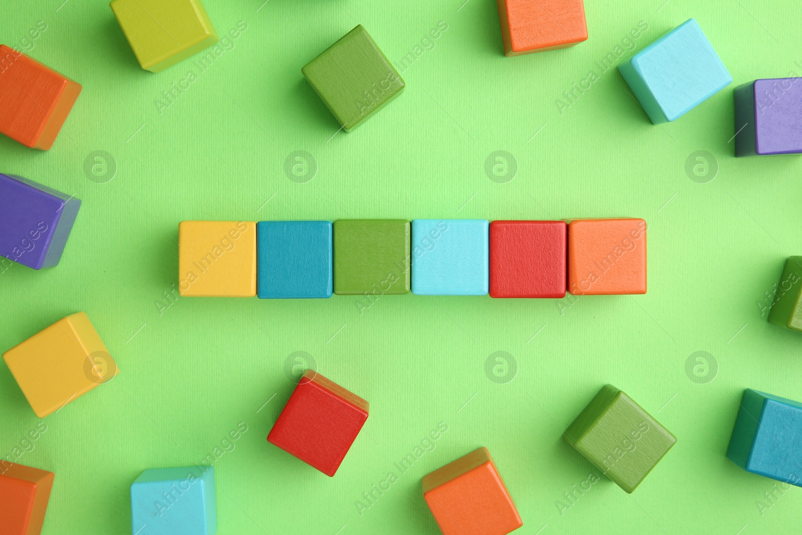 Photo of Many wooden colorful cubes on green background, top view