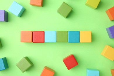 Photo of Many wooden colorful cubes on green background, top view