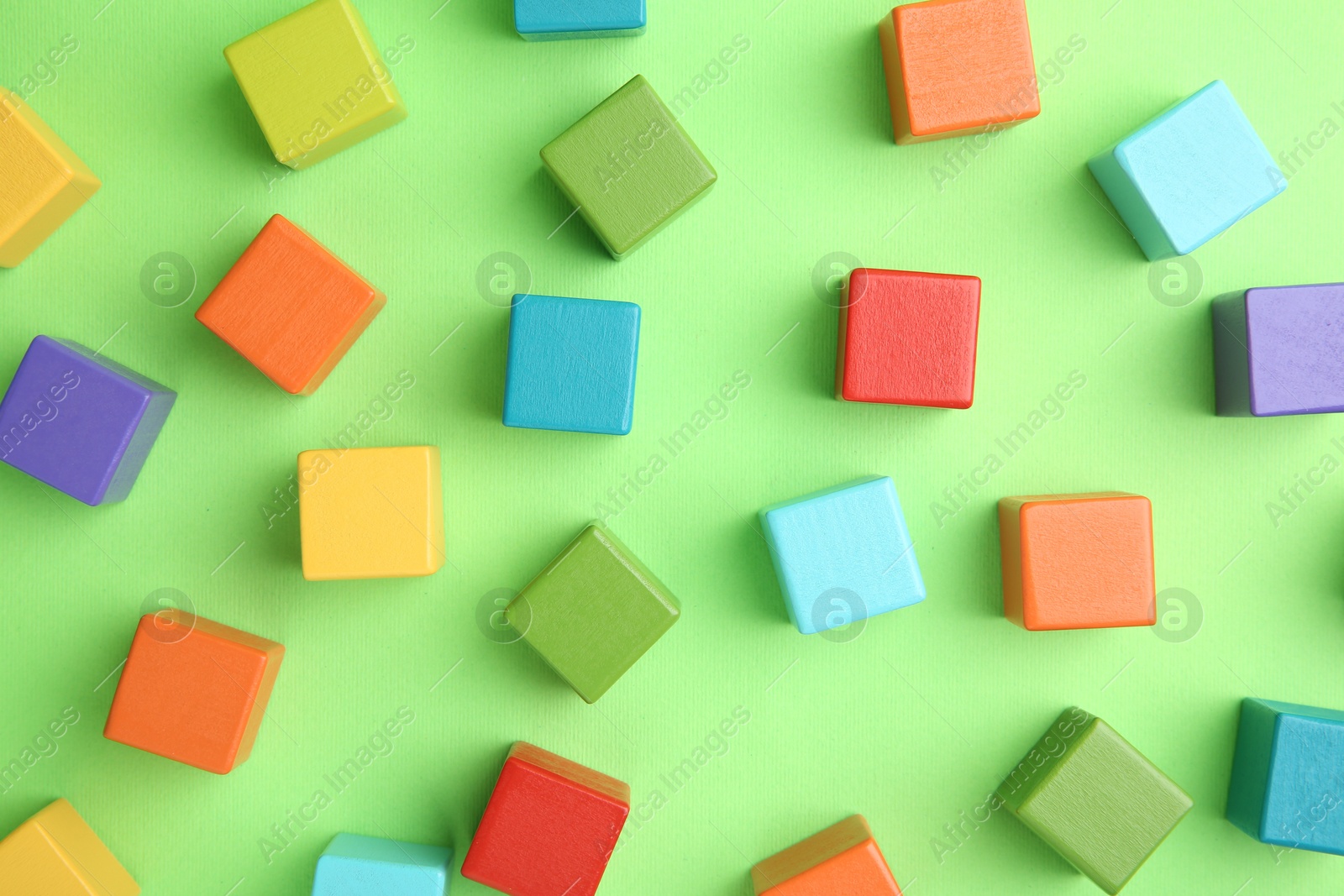 Photo of Many wooden colorful cubes on green background, top view