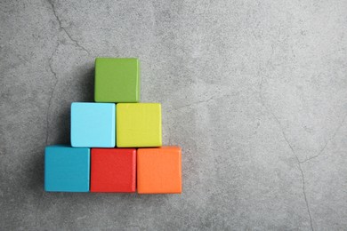 Photo of Pyramid of colorful cubes on gray textured background, top view. Space for text