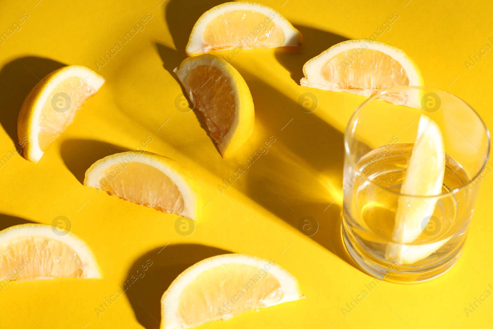 Photo of Fresh lemon slices and glass on yellow background