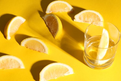 Fresh lemon slices and glass on yellow background