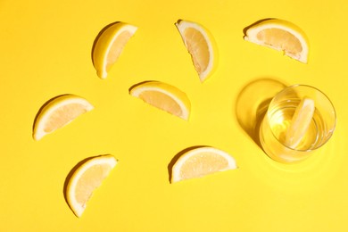 Fresh lemon slices and glass on yellow background, flat lay