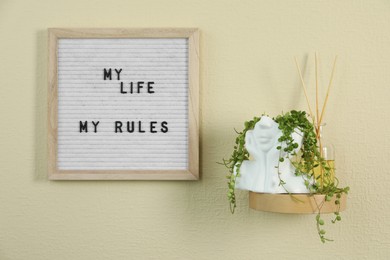 Photo of Letter board with phrase My Life My Rules, reed diffuser and plant on beige wall