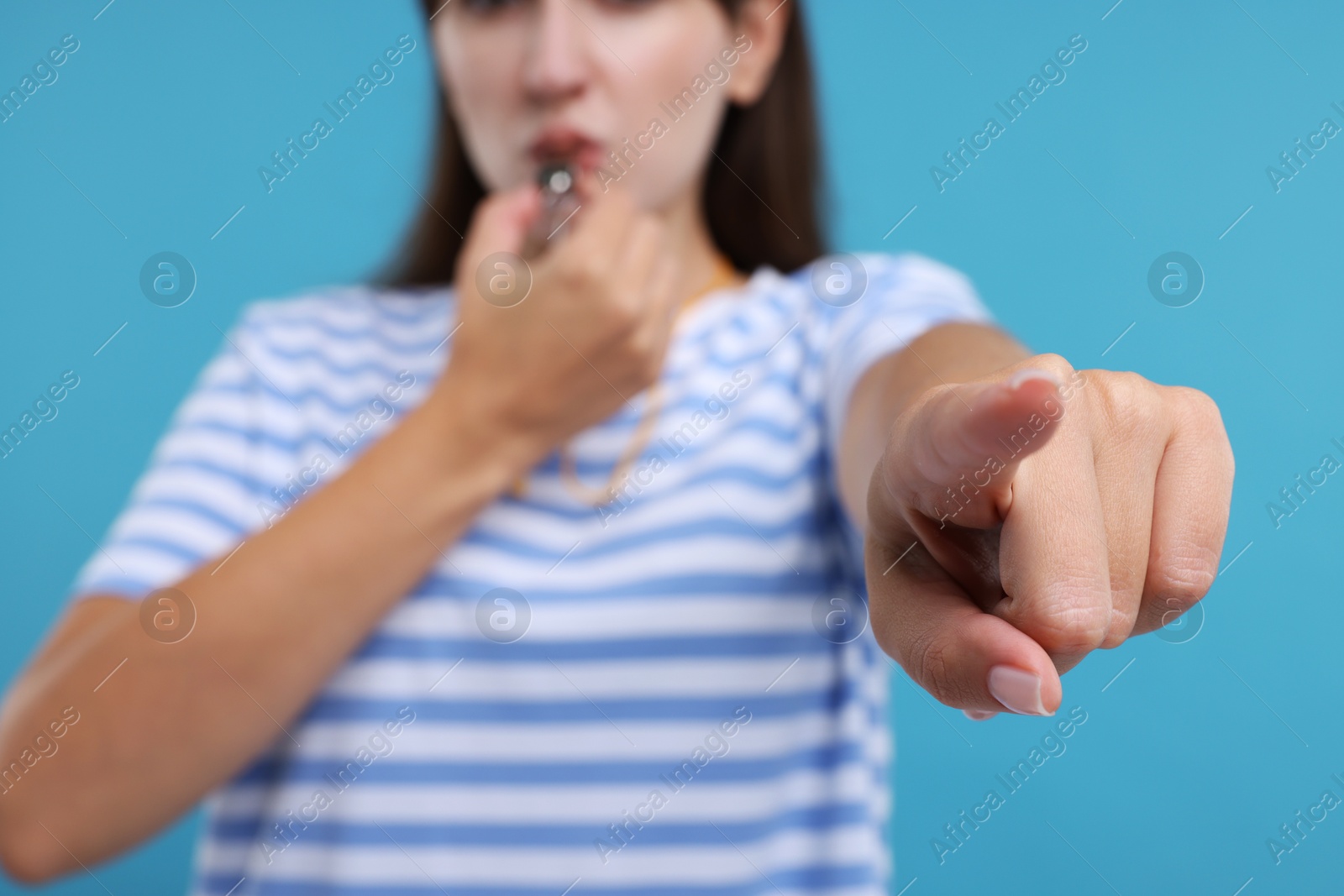 Photo of Woman blowing whistle on light blue background, closeup