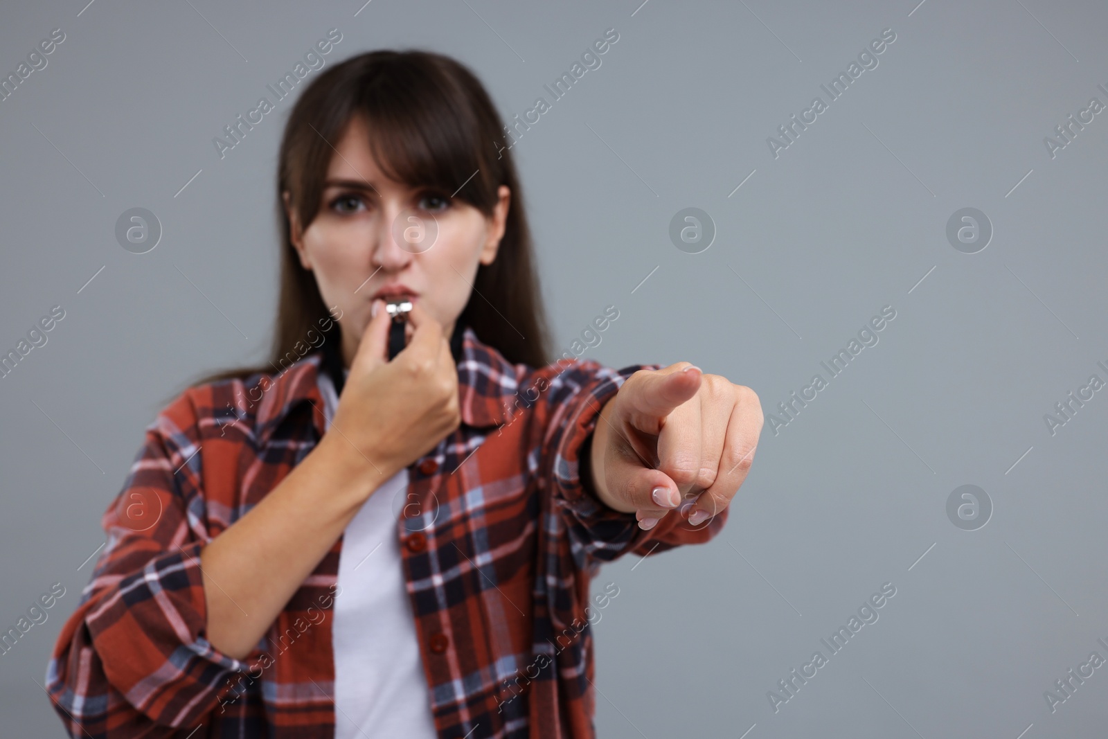 Photo of Woman blowing whistle on grey background, selective focus. Space for text