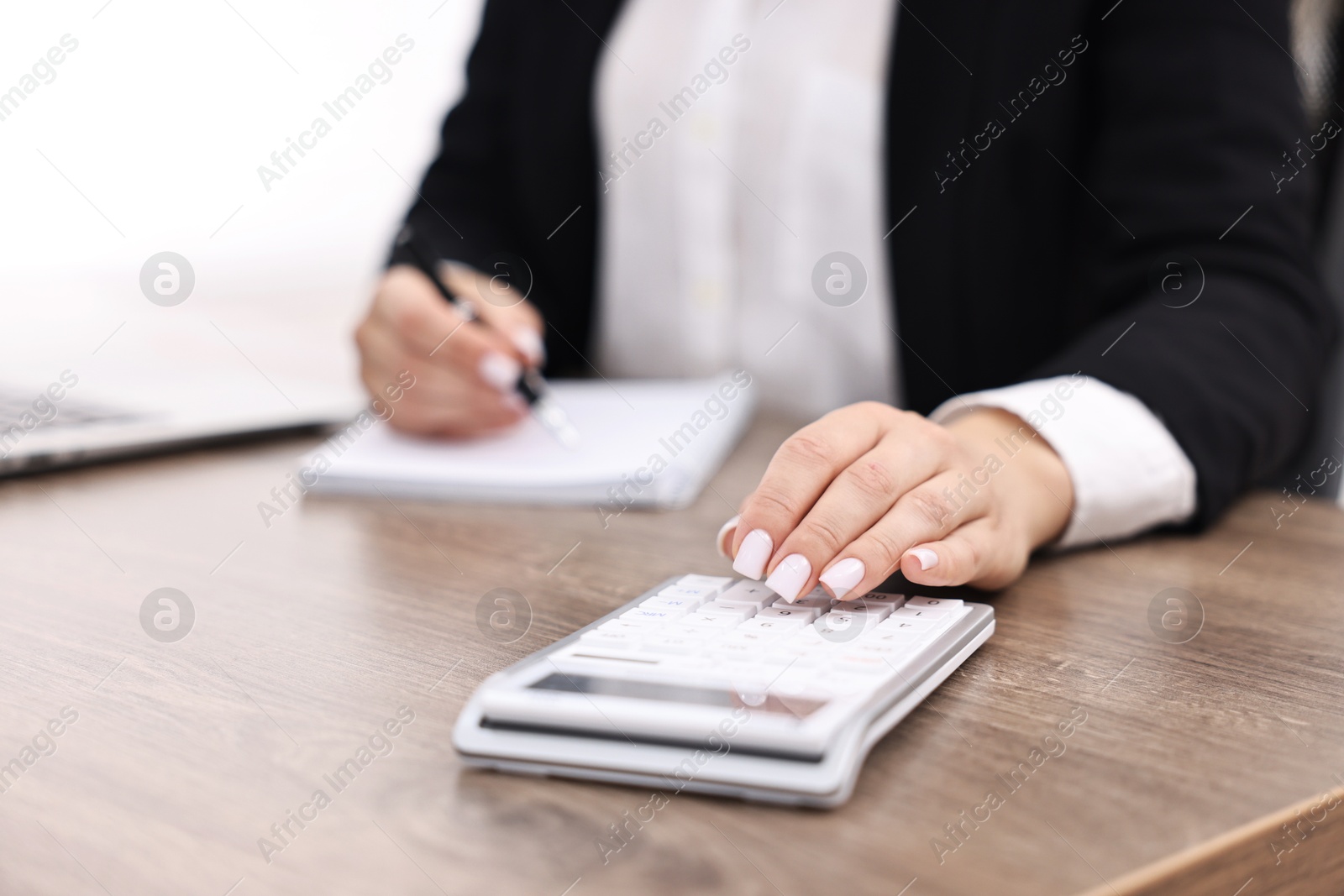 Photo of Banker with notebook using calculator at wooden table in office, closeup