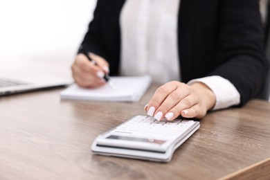 Banker with notebook using calculator at wooden table in office, closeup