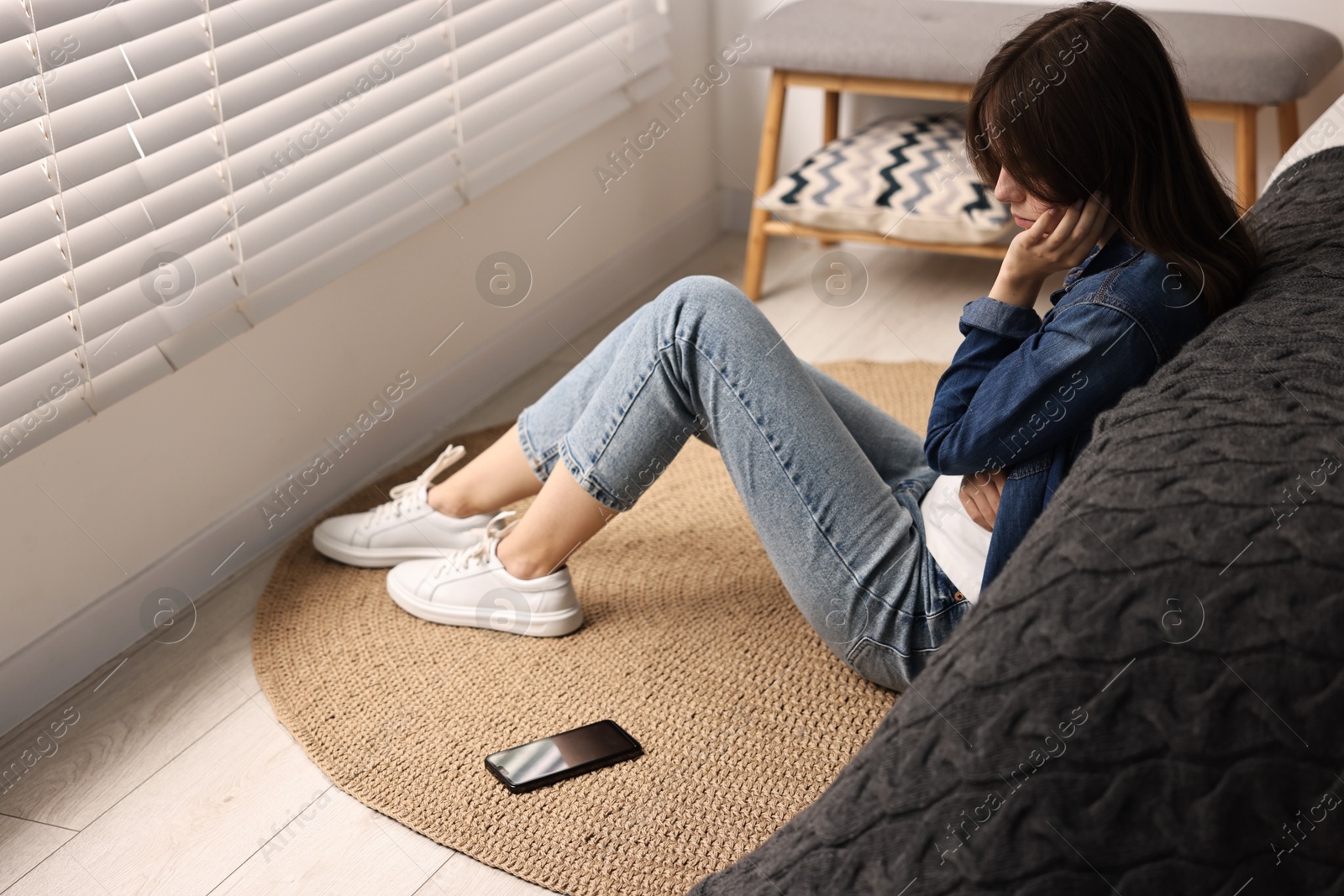 Photo of Loneliness concept. Sad teenage girl with smartphone on floor at home