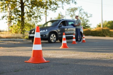 Examiner instructing student before exam at driving school test track, focus on traffic cone