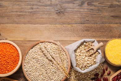 Photo of Different types of cereals and legumes on wooden table, flat lay. Space for text