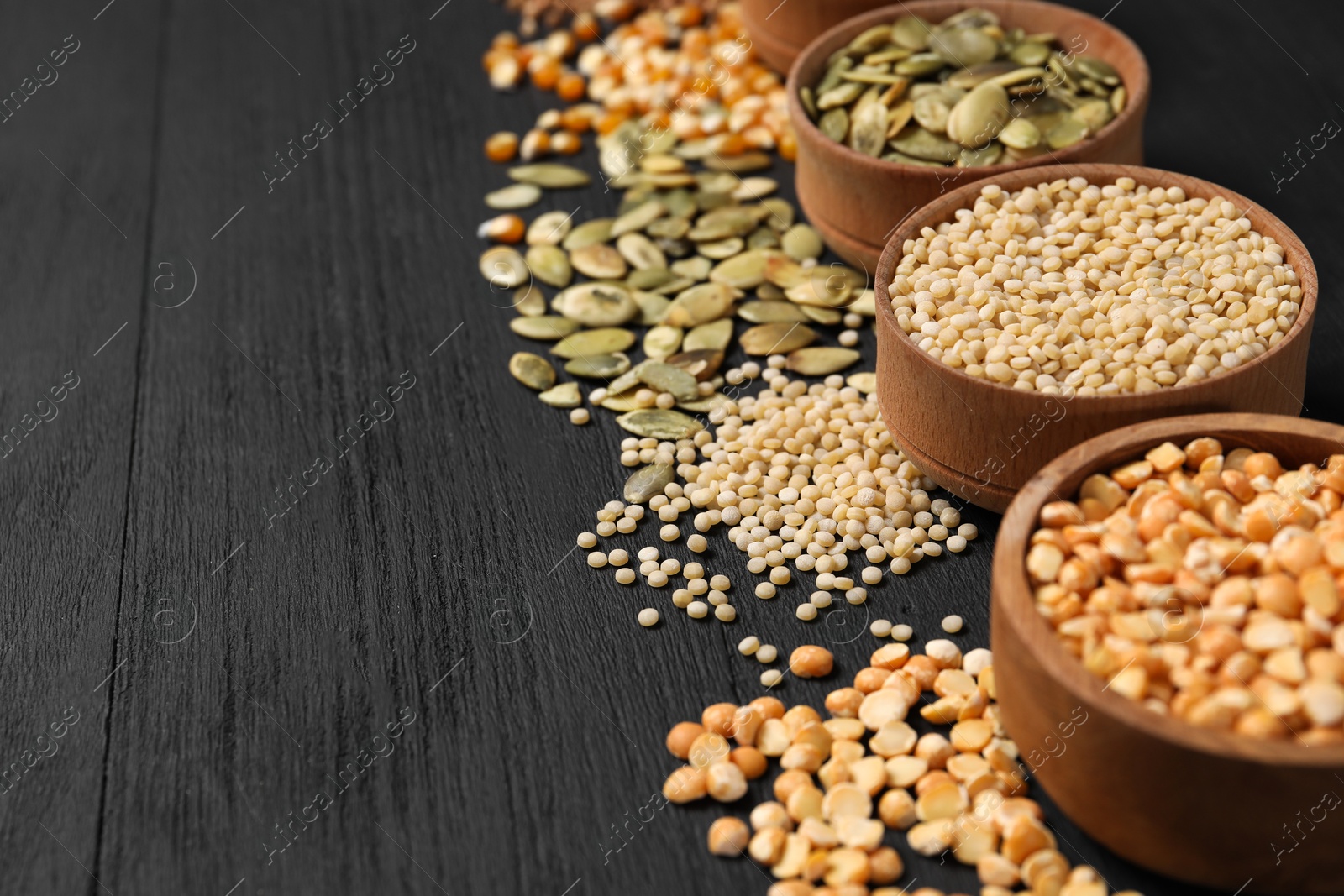 Photo of Different types of seeds and cereals in bowls on black wooden table, closeup. Space for text